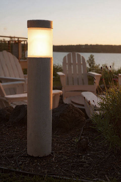 Outdoor landscape light made of concrete with a scenic background of chairs and water.