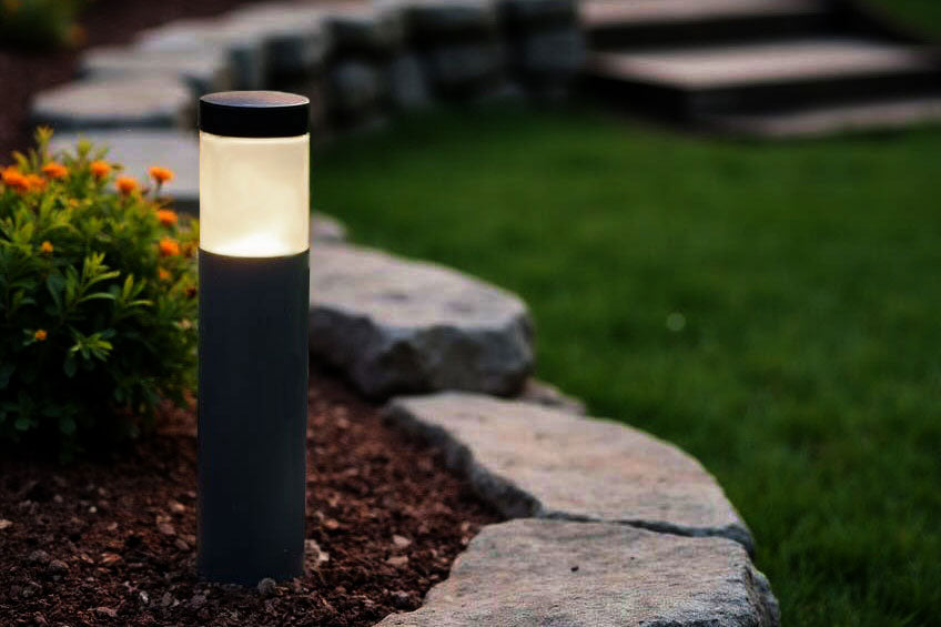 Concrete light post on a stone pathway with grass and plants in the background