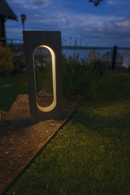 Modern outdoor garden light fixture on a grassy area with a body of water in the background.